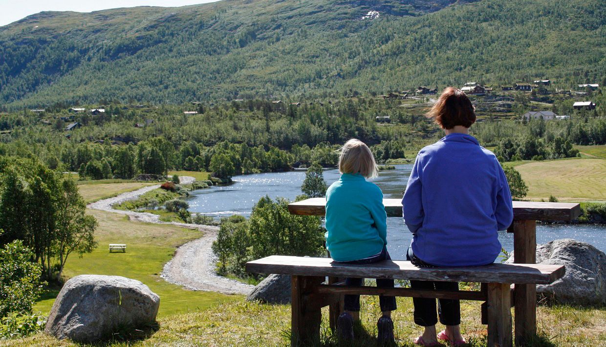 A woman and a child enjoying the river view on a bench.