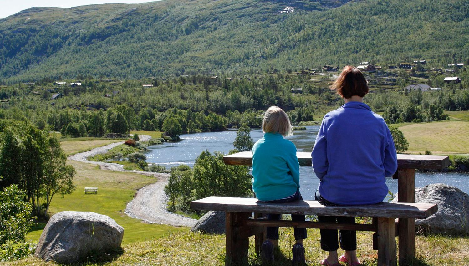 A woman and a child enjoying the river view on a bench.