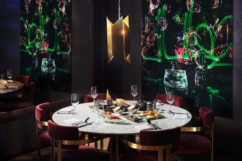 Restaurantinteriør med gullampe, rundt, hvitt bord og røde stoler, med vinglass, bestikk og mat.