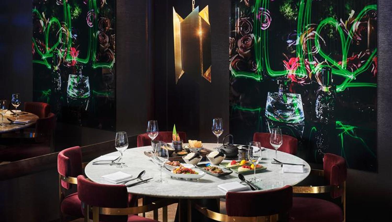 Restaurantinteriør med gullampe, rundt, hvitt bord og røde stoler, med vinglass, bestikk og mat.