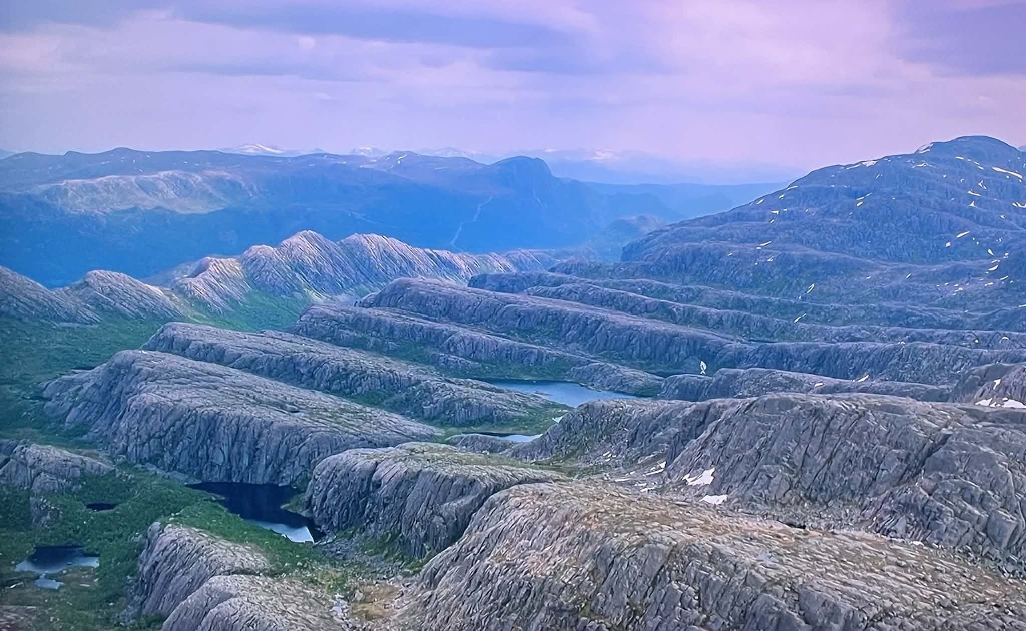 Opplevingar i nærleiken av Bremanger Fjordhotell: Utsyn over steinete fjellryggar i Ålfoten med små vatn og snøflekker, med blå fjell i bakgrunnen under skya himmel..
