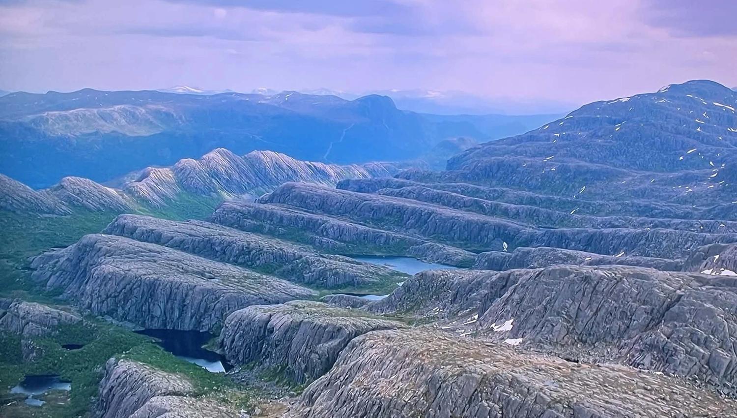Opplevingar i nærleiken av Bremanger Fjordhotell: Utsyn over steinete fjellryggar i Ålfoten med små vatn og snøflekker, med blå fjell i bakgrunnen under skya himmel..