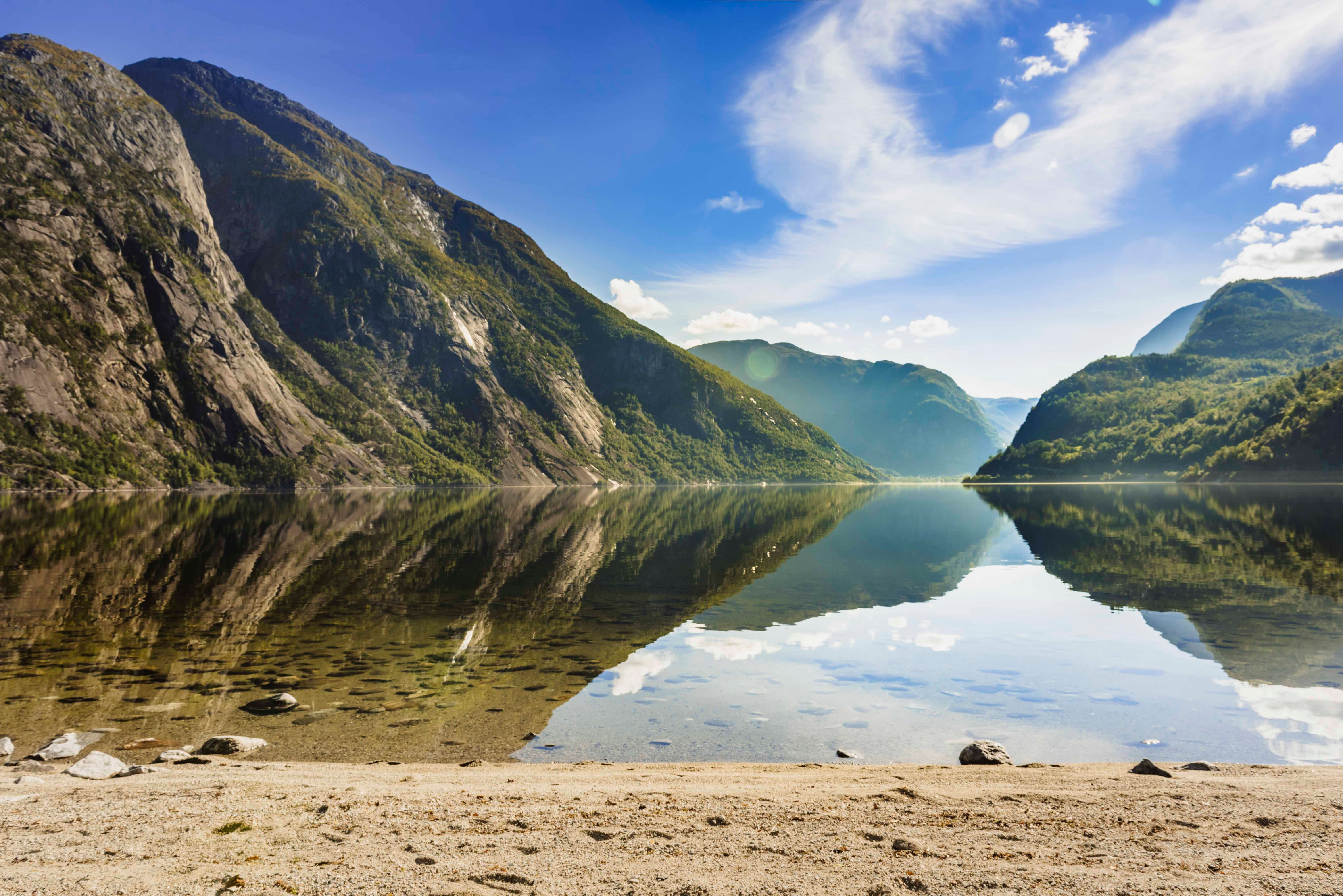 The sandy beach by the Eidfjord lake. The mountains surrounding the lake is reflecting perfectly in the lake.