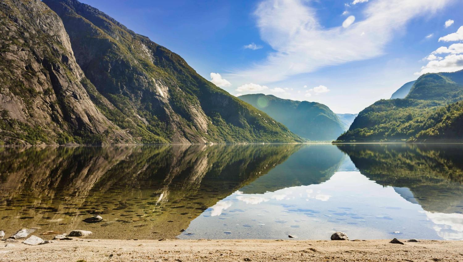 The sandy beach by the Eidfjord lake. The mountains surrounding the lake is reflecting perfectly in the lake.