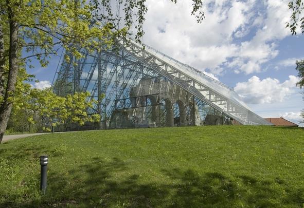 Hamardomen på Domkirkeodden
En stor bygning med glassfasade ligger bak en gressbakke under blå himmel og skyer.