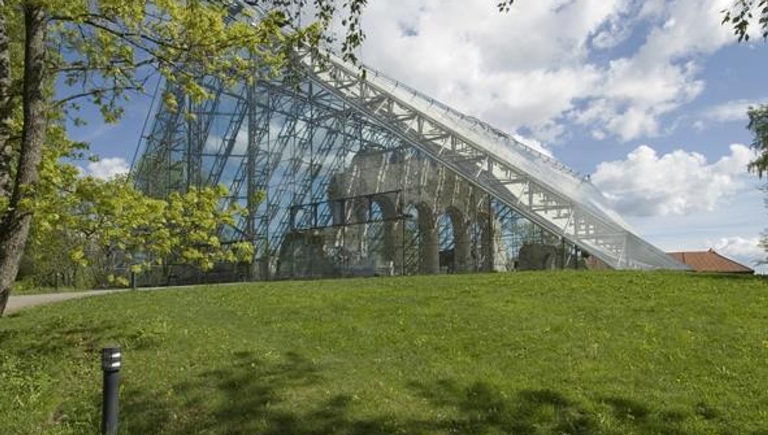 Hamardomen på Domkirkeodden
En stor bygning med glassfasade ligger bak en gressbakke under blå himmel og skyer.