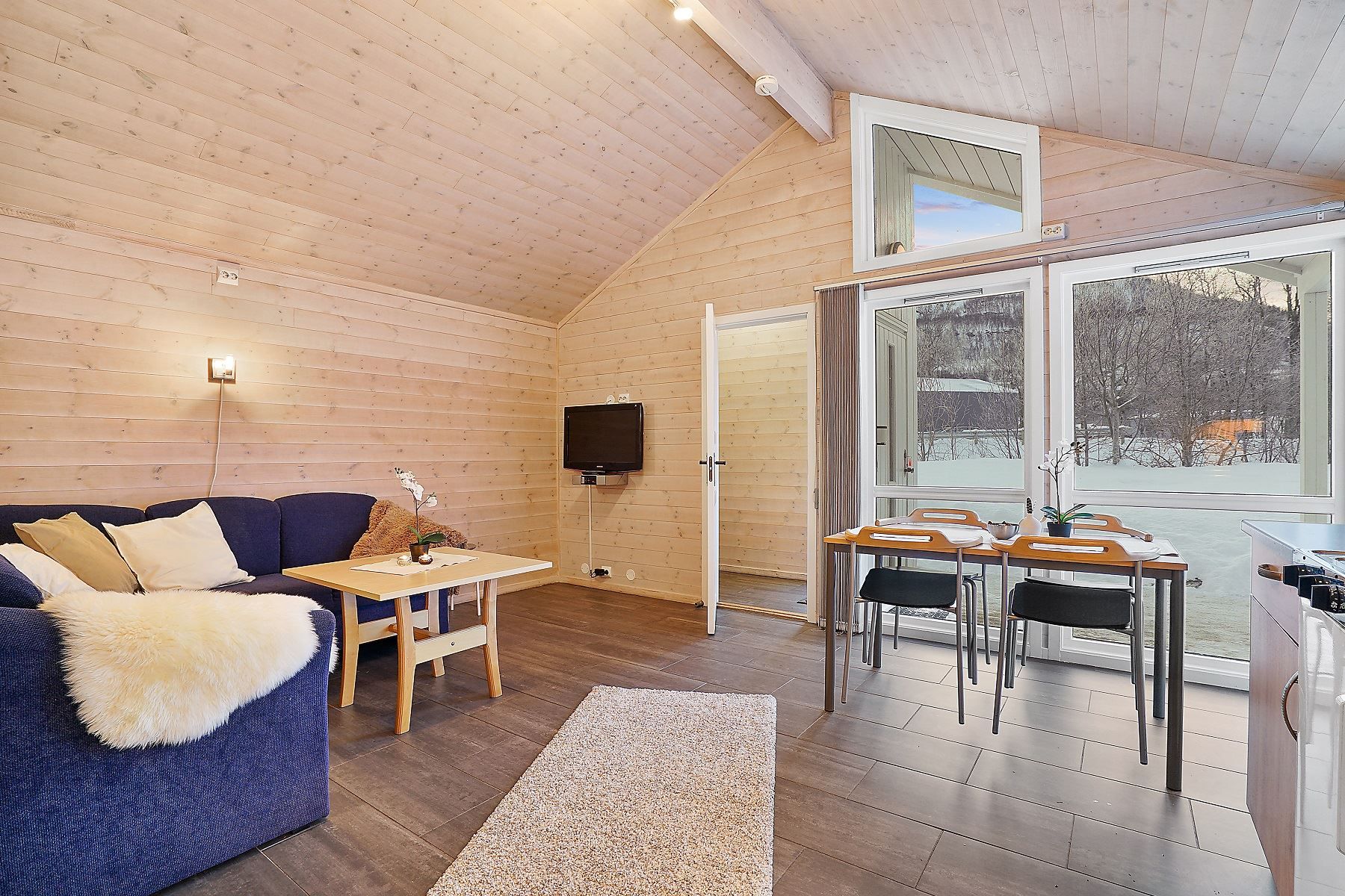 Cosy living room with blue sofa, dining table, and large windows facing snowy scenery