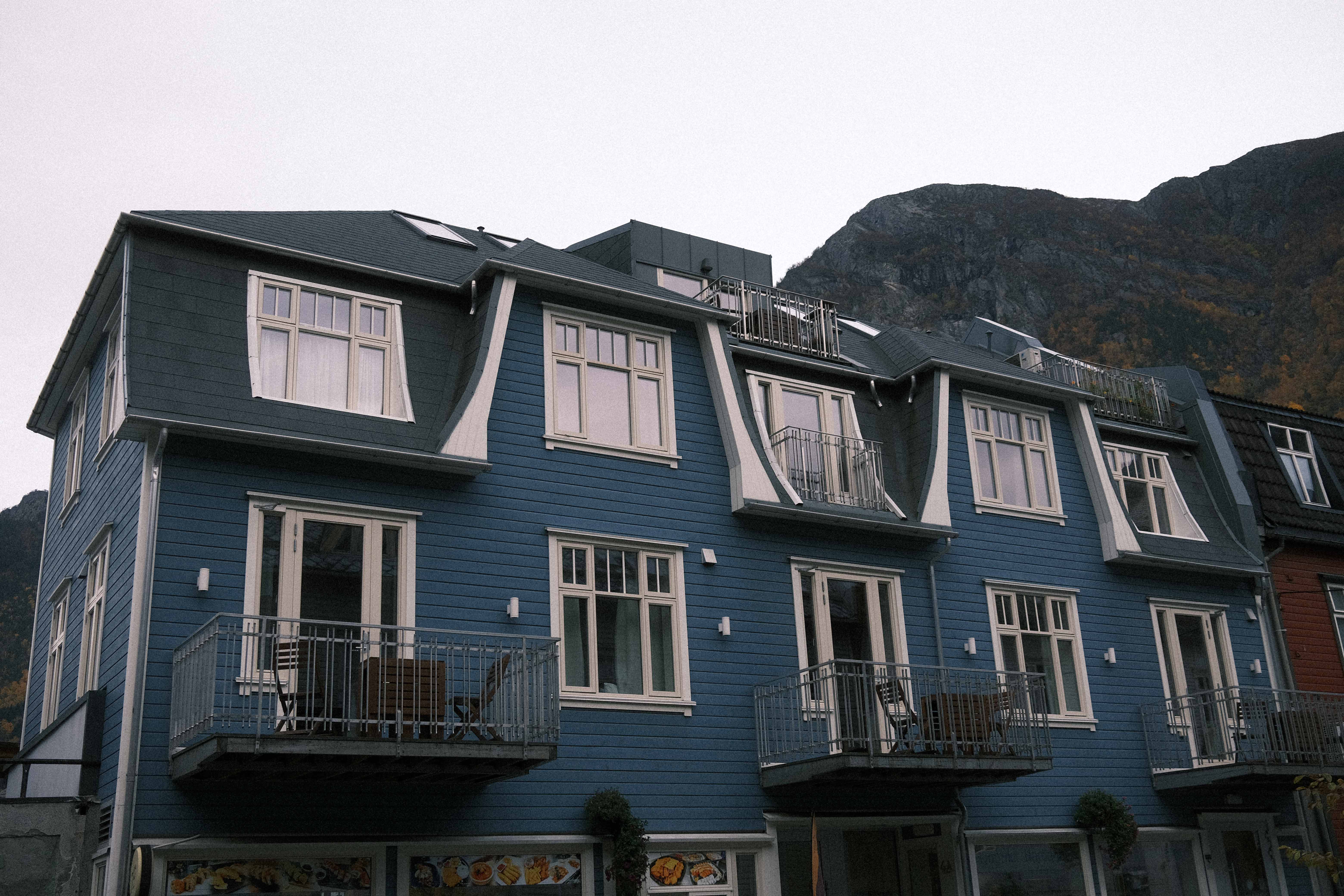 The blue exterior of Blue House Odda with mountain scenery in the background, centrally located in Odda.