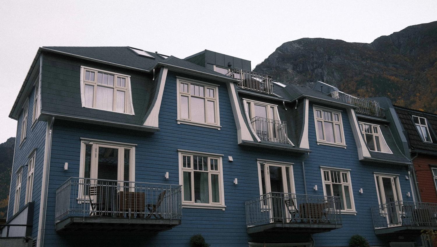 The blue exterior of Blue House Odda with mountain scenery in the background, centrally located in Odda.