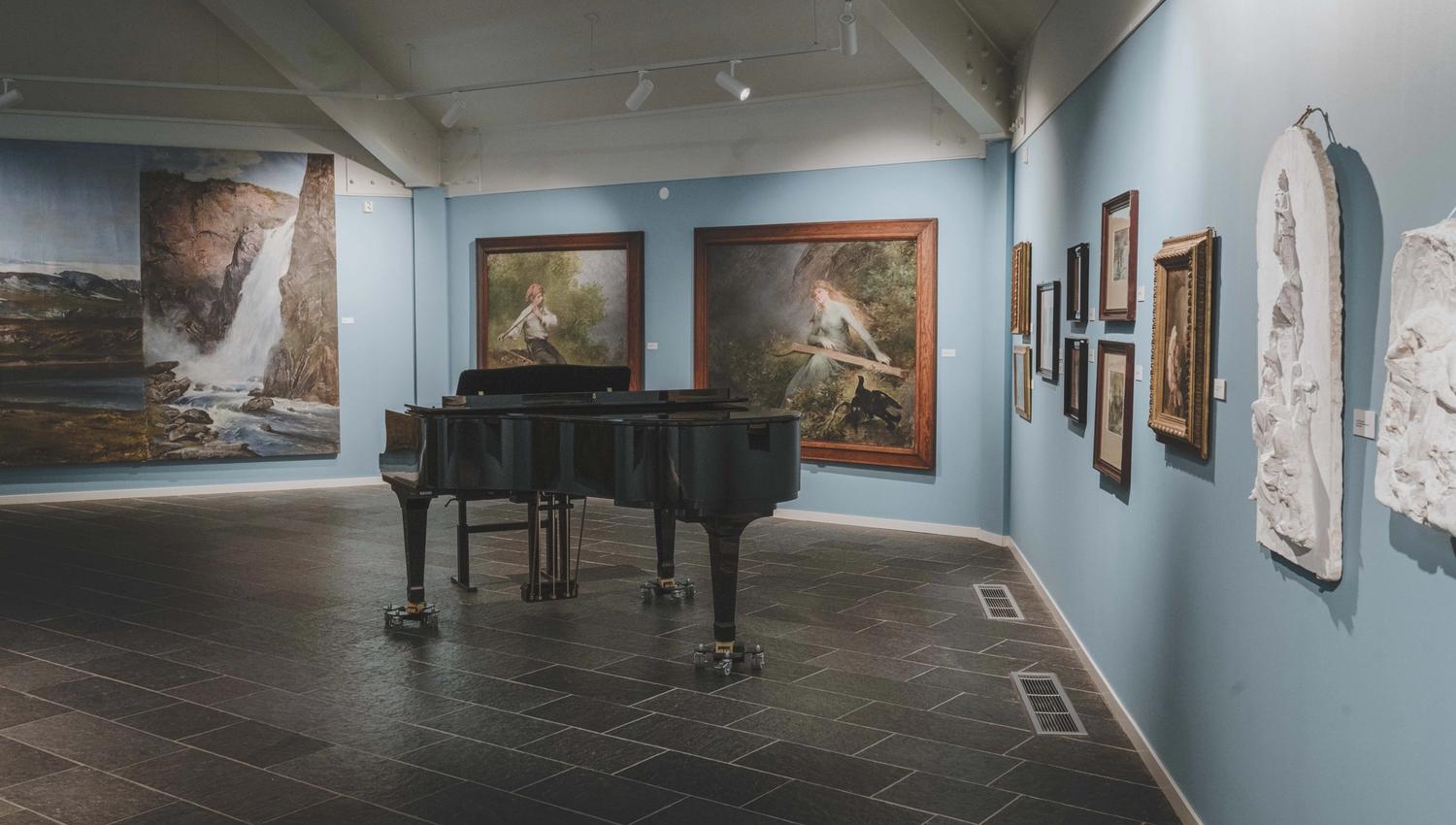 A baby grand piano in front of some of Bergsliens paintings.