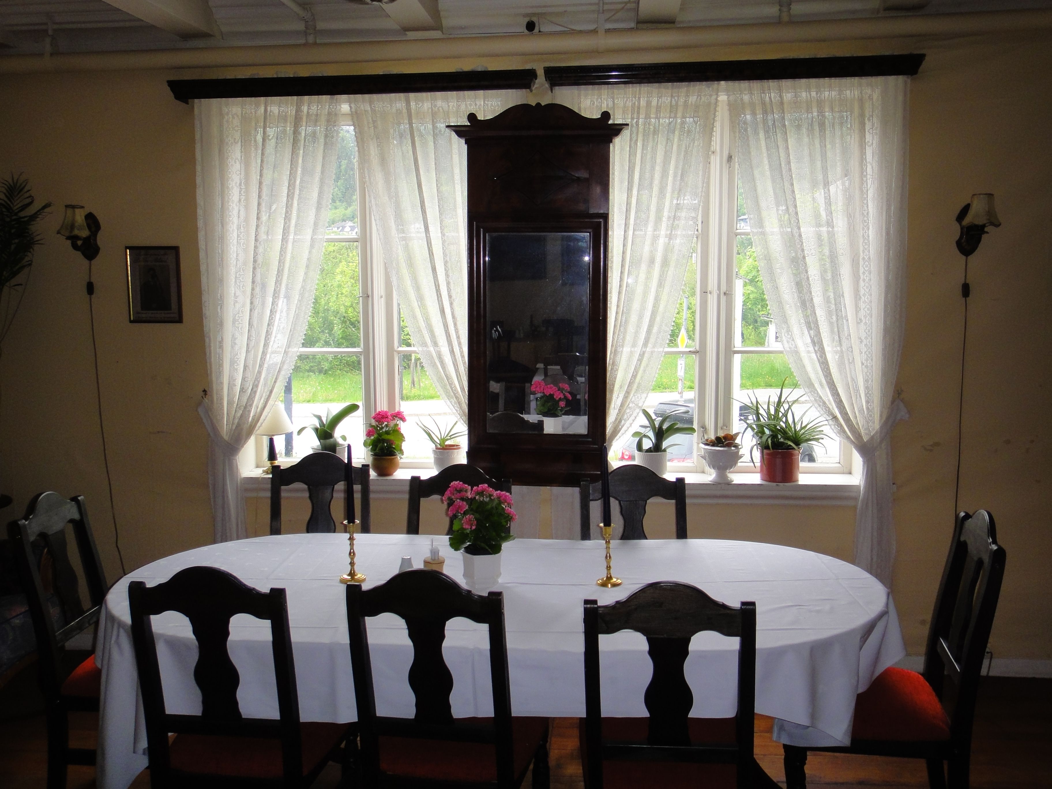 Bright and inviting dining room with white tablecloth, antique chairs and garden view at Jaunsen Guesthouse in Hardanger, Norway.