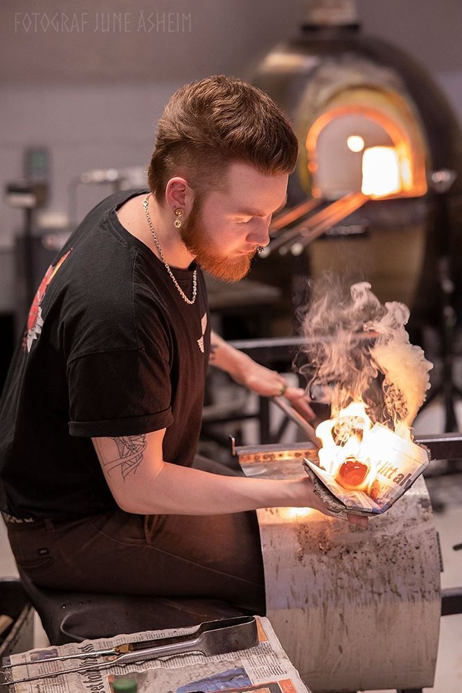Glassblower working with glowing molten glass at Blåst Glass Studio in Tromsø, combining traditional craftsmanship with creative glass art.