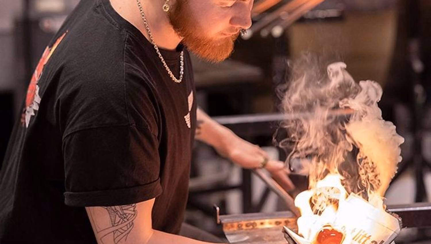 Glassblower working with glowing molten glass at Blåst Glass Studio in Tromsø, combining traditional craftsmanship with creative glass art.