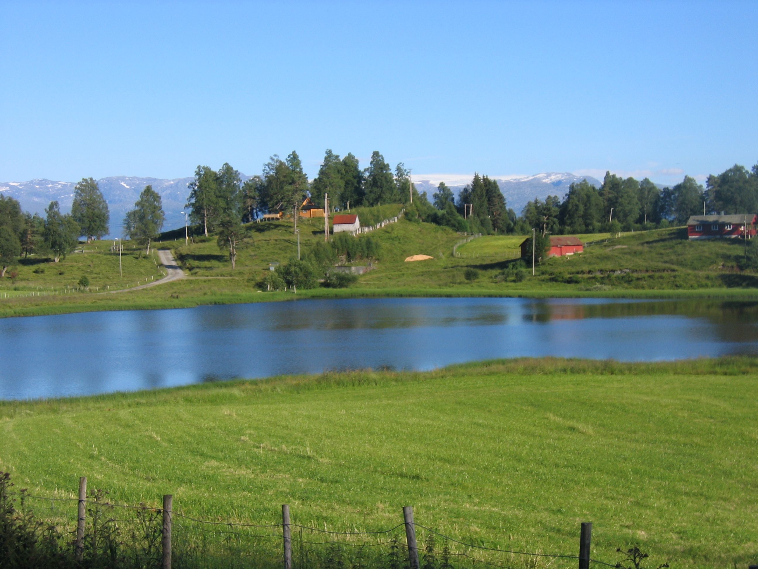Mirror-like lake surrounded by green fields and mountains in Hardanger.