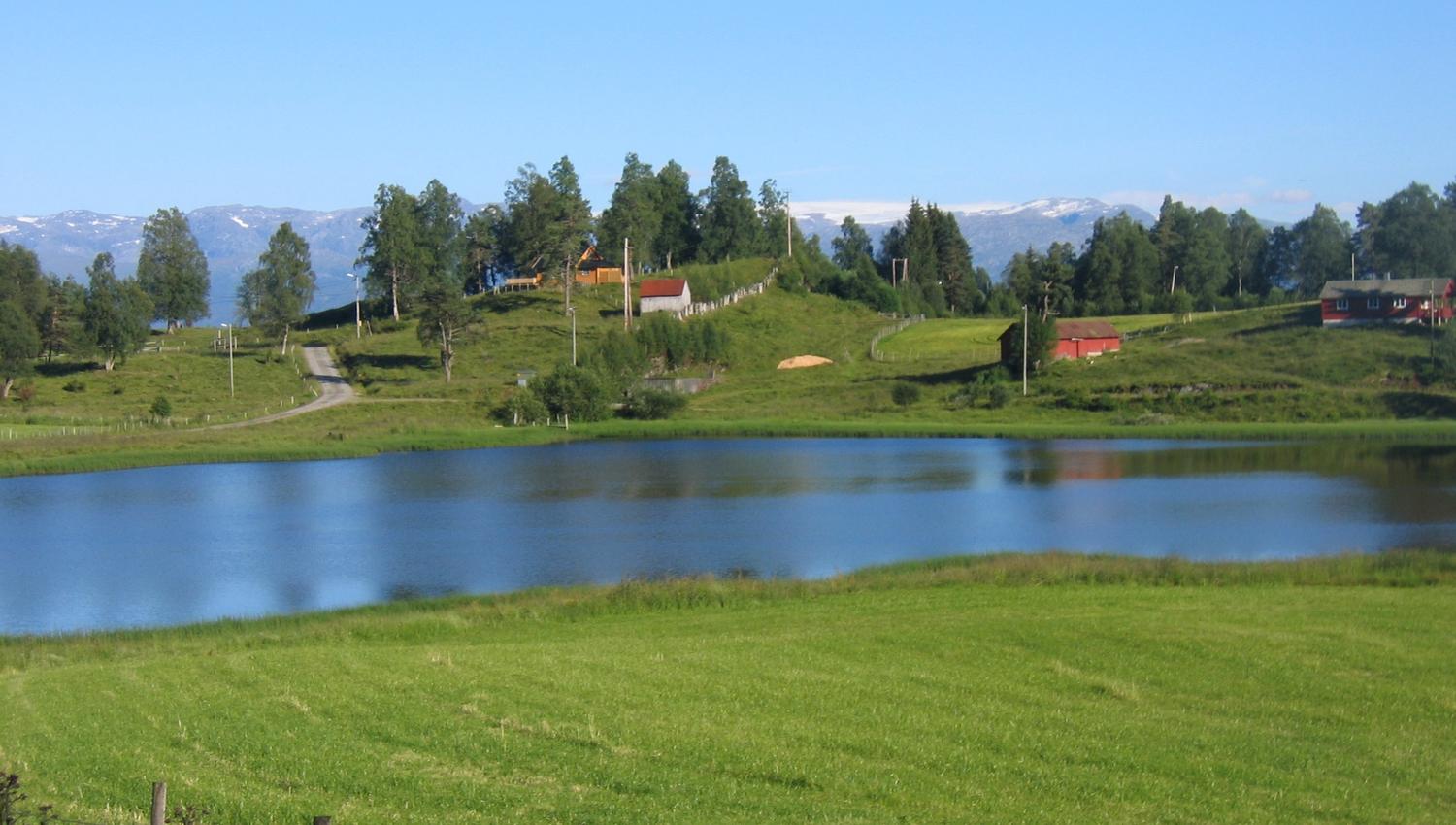 Mirror-like lake surrounded by green fields and mountains in Hardanger.
