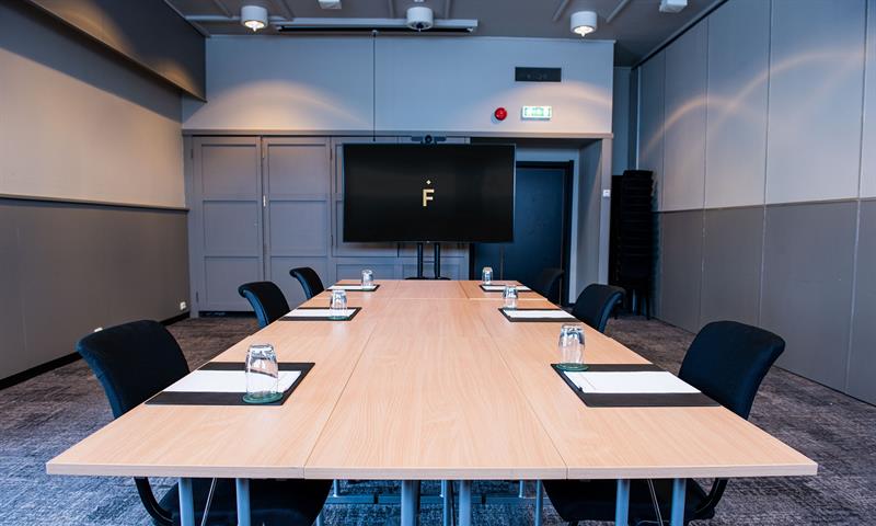 A conference room with chairs surrounding a long table with big screen in the background