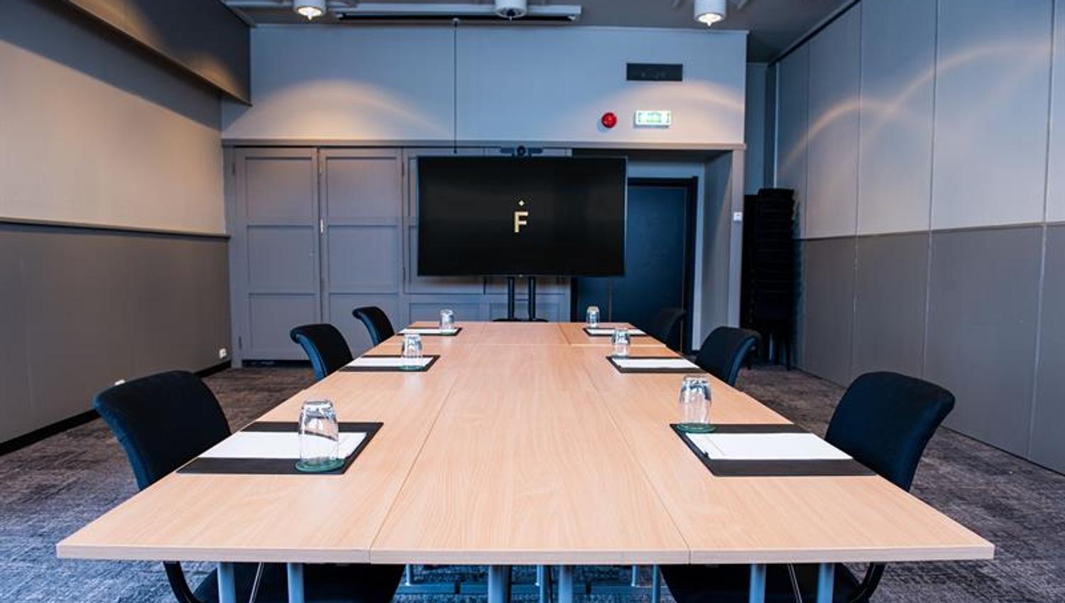 A conference room with chairs surrounding a long table with big screen in the background
