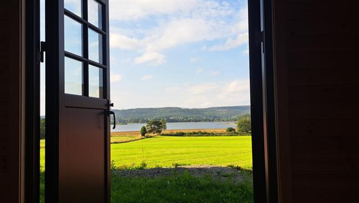 Open door framing green fields, a lake and forested hills in a peaceful countryside