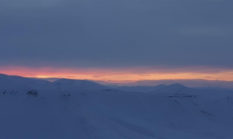 A snow-covered landscape with low clouds and a thin stripe of light from a sunset far in the background