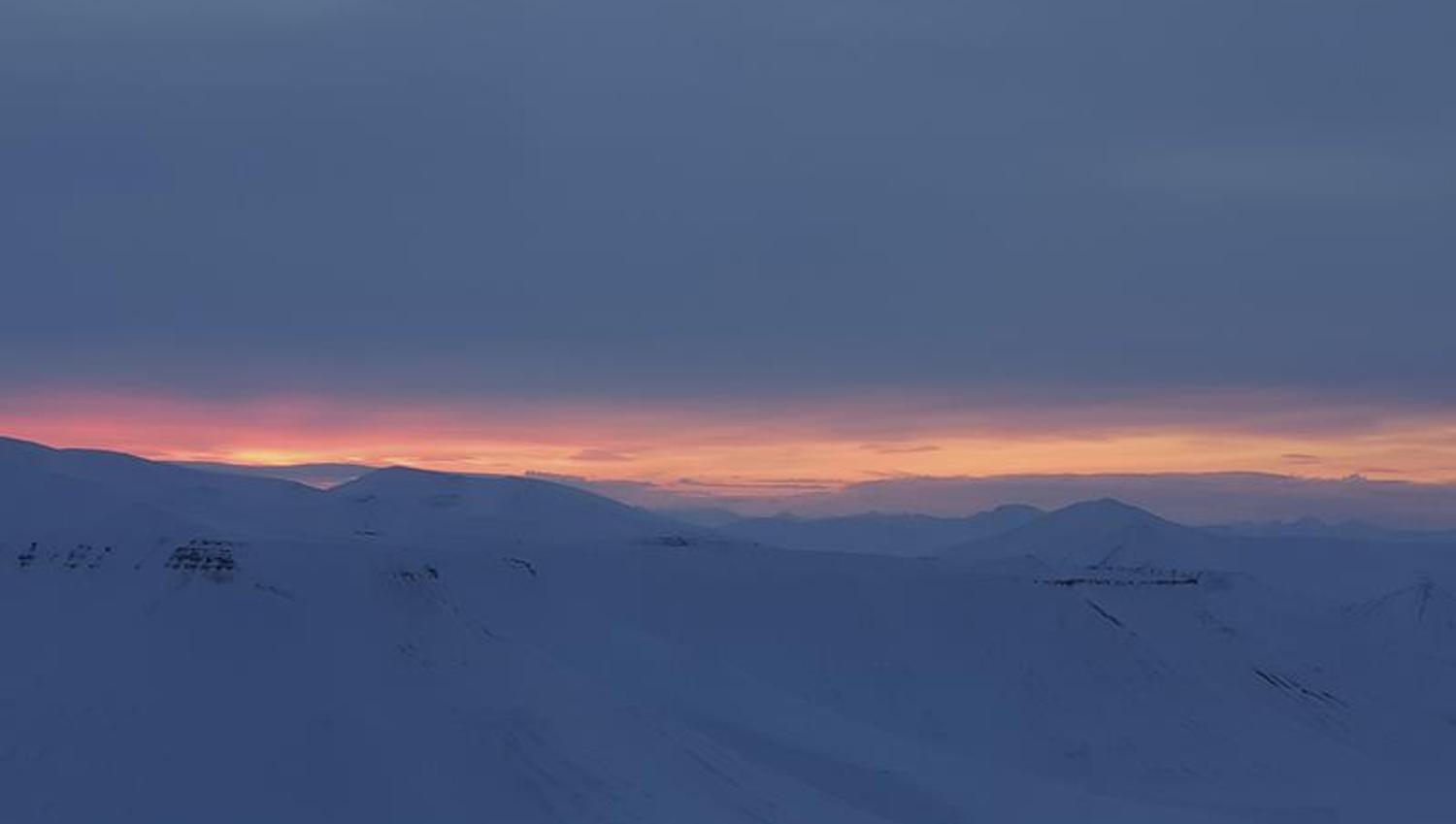 A snow-covered landscape with low clouds and a thin stripe of light from a sunset far in the background