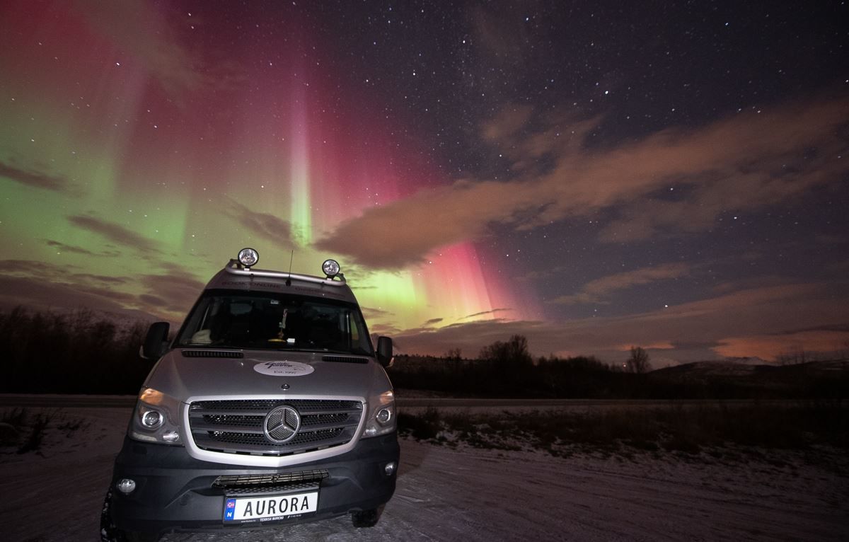 Northern Lights shines behind the tour bus, with "AURORA" on its number plate