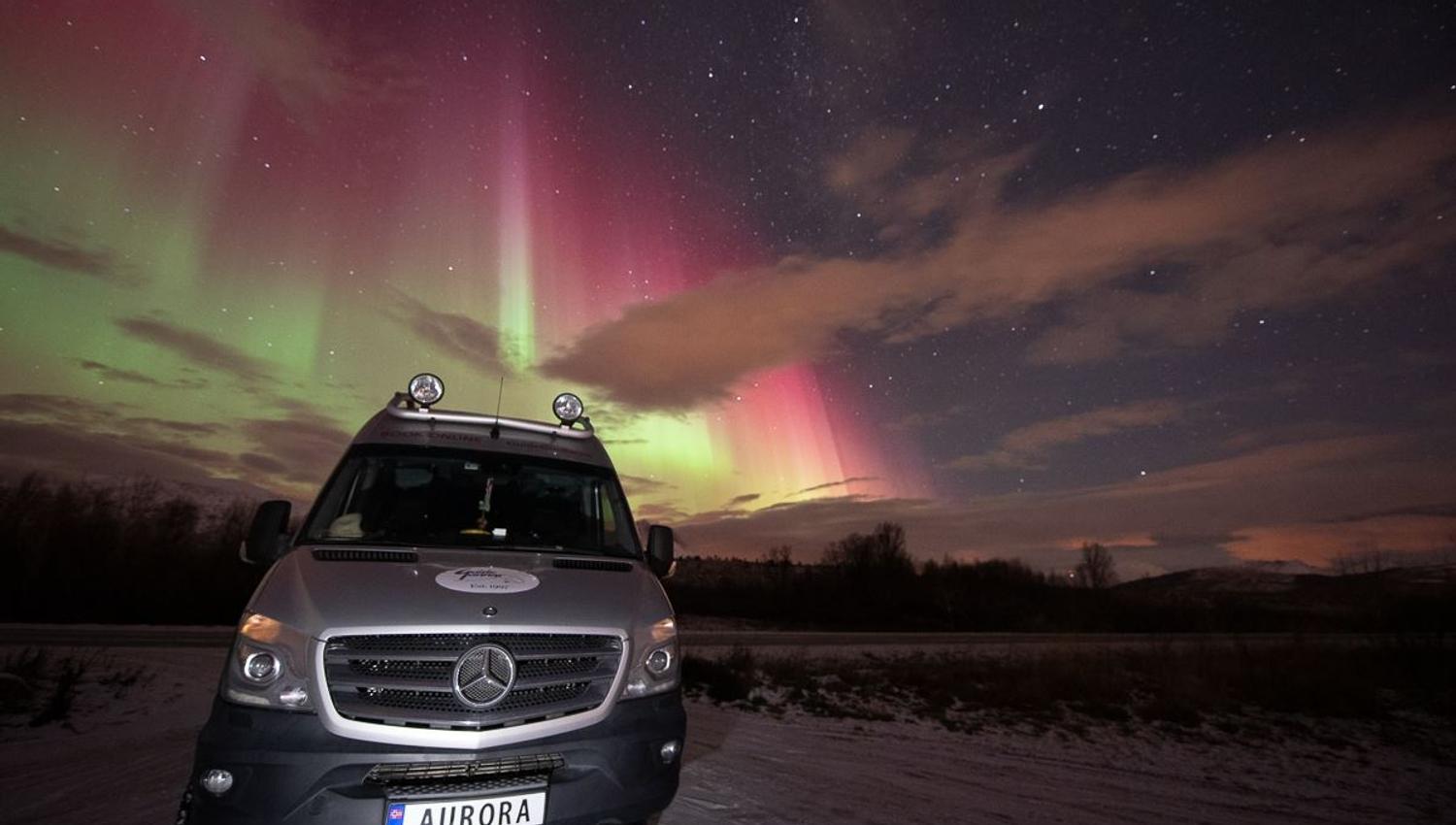 Northern Lights shines behind the tour bus, with "AURORA" on its number plate