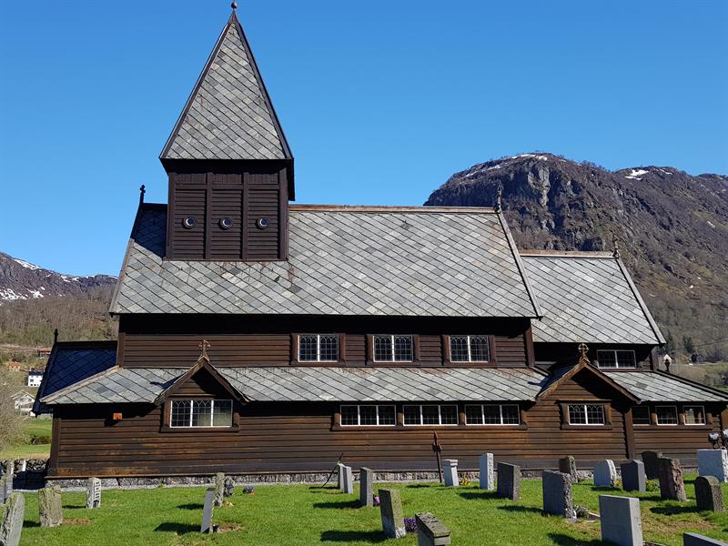 Røldal Stave Church in the spring sun with snowy mountain peaks – a beautiful meeting of culture and nature.