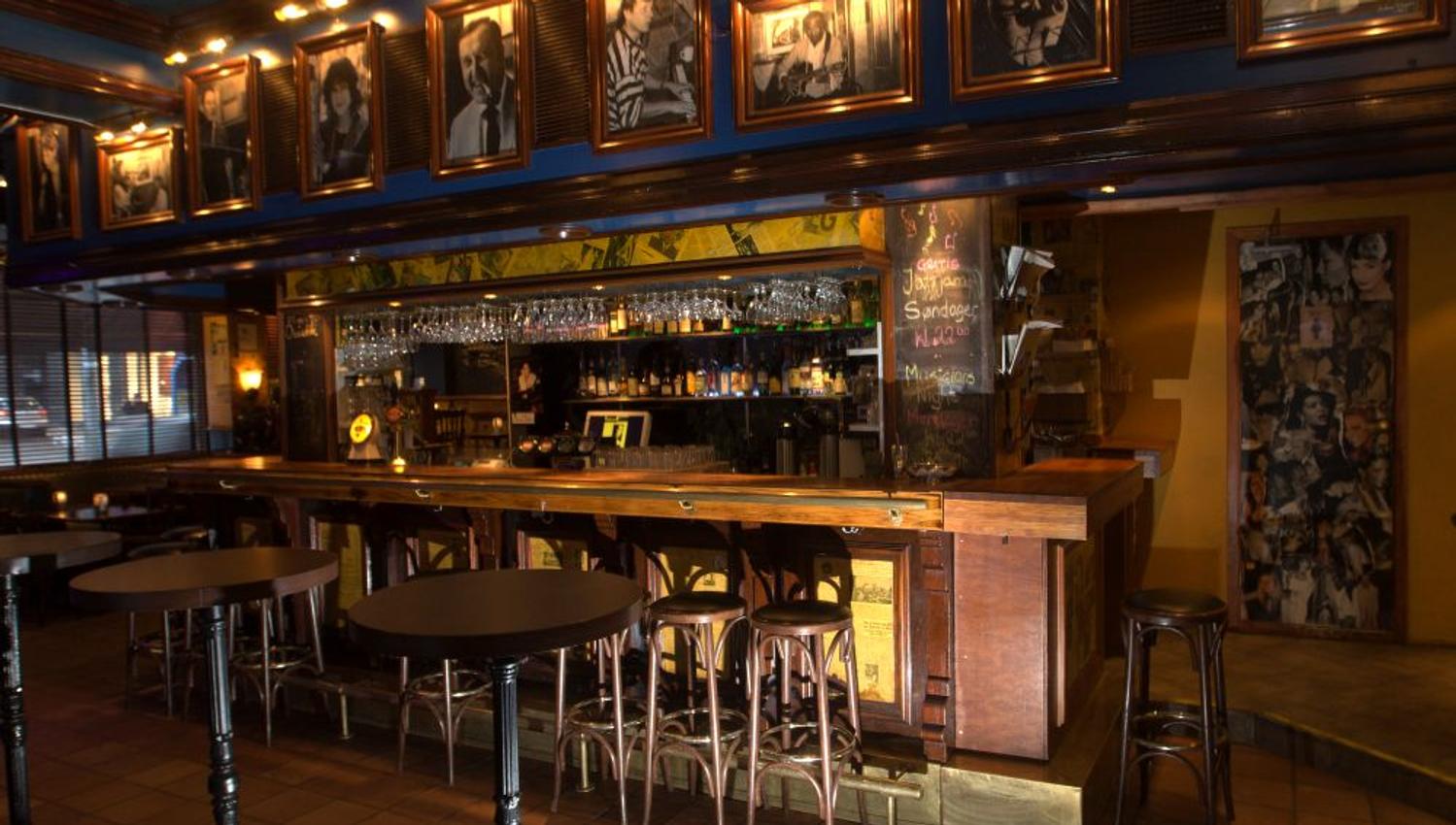 Interior of bar area with counter, bar stools and a number of photos above the bar.