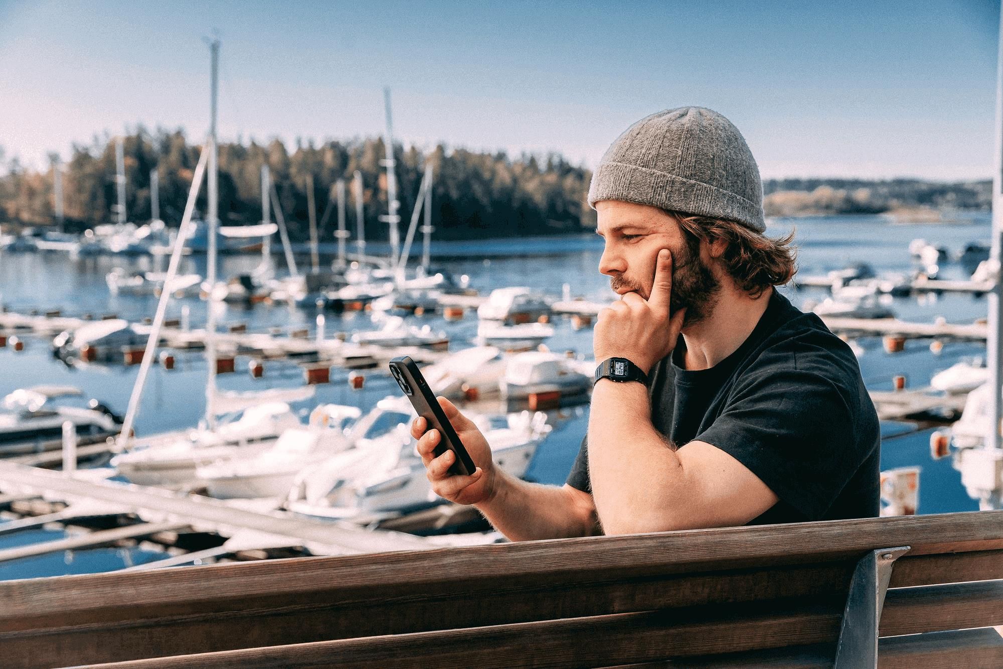 Man looking at the phone in front of a marina with many boats