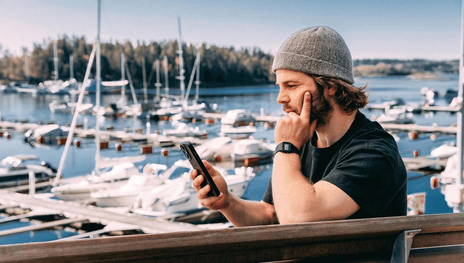 Man looking at the phone in front of a marina with many boats