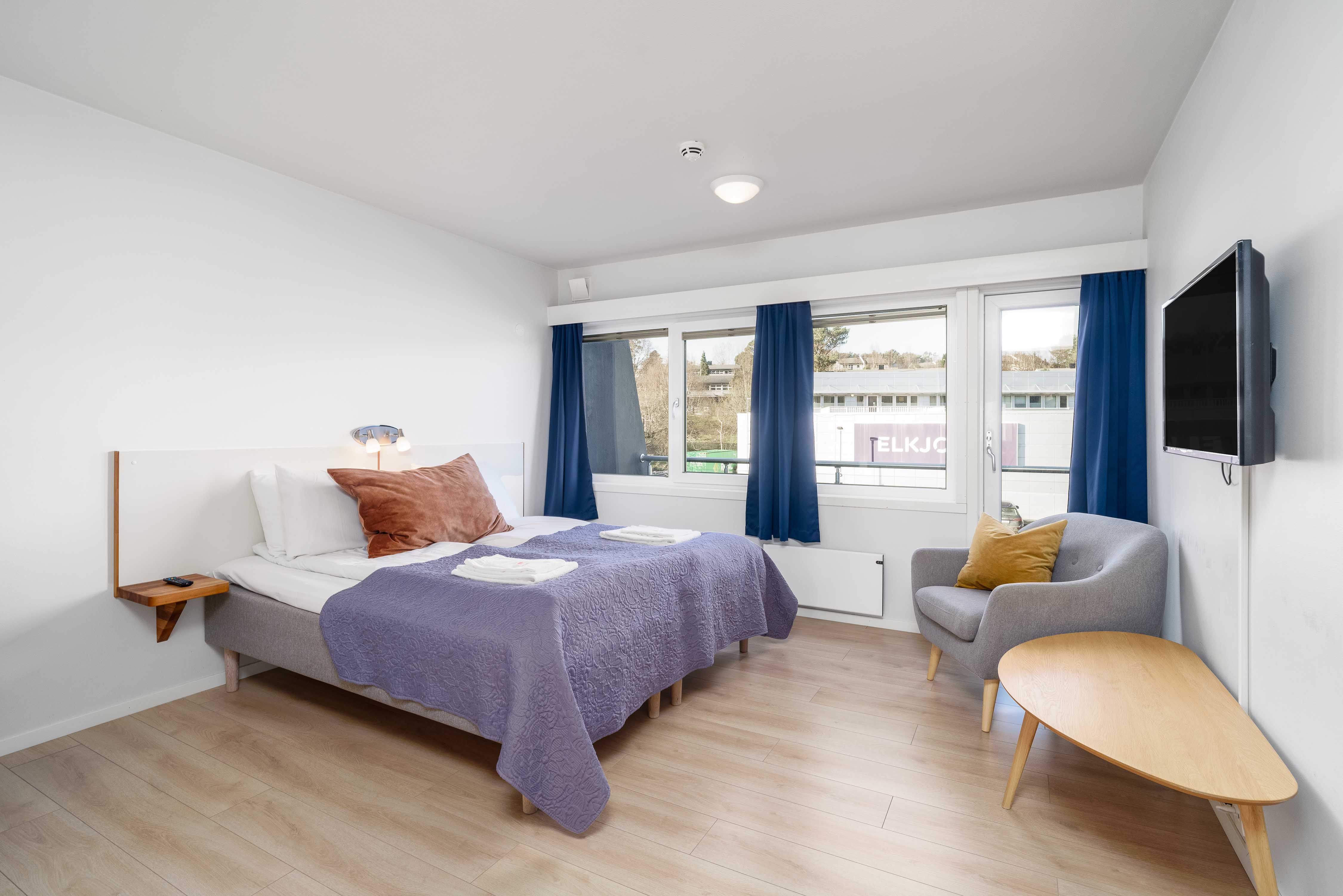 Lyst og innbydande hotellrom på Husnes Sentrum Hotell med store vindauge og avslappa atmosfære.
