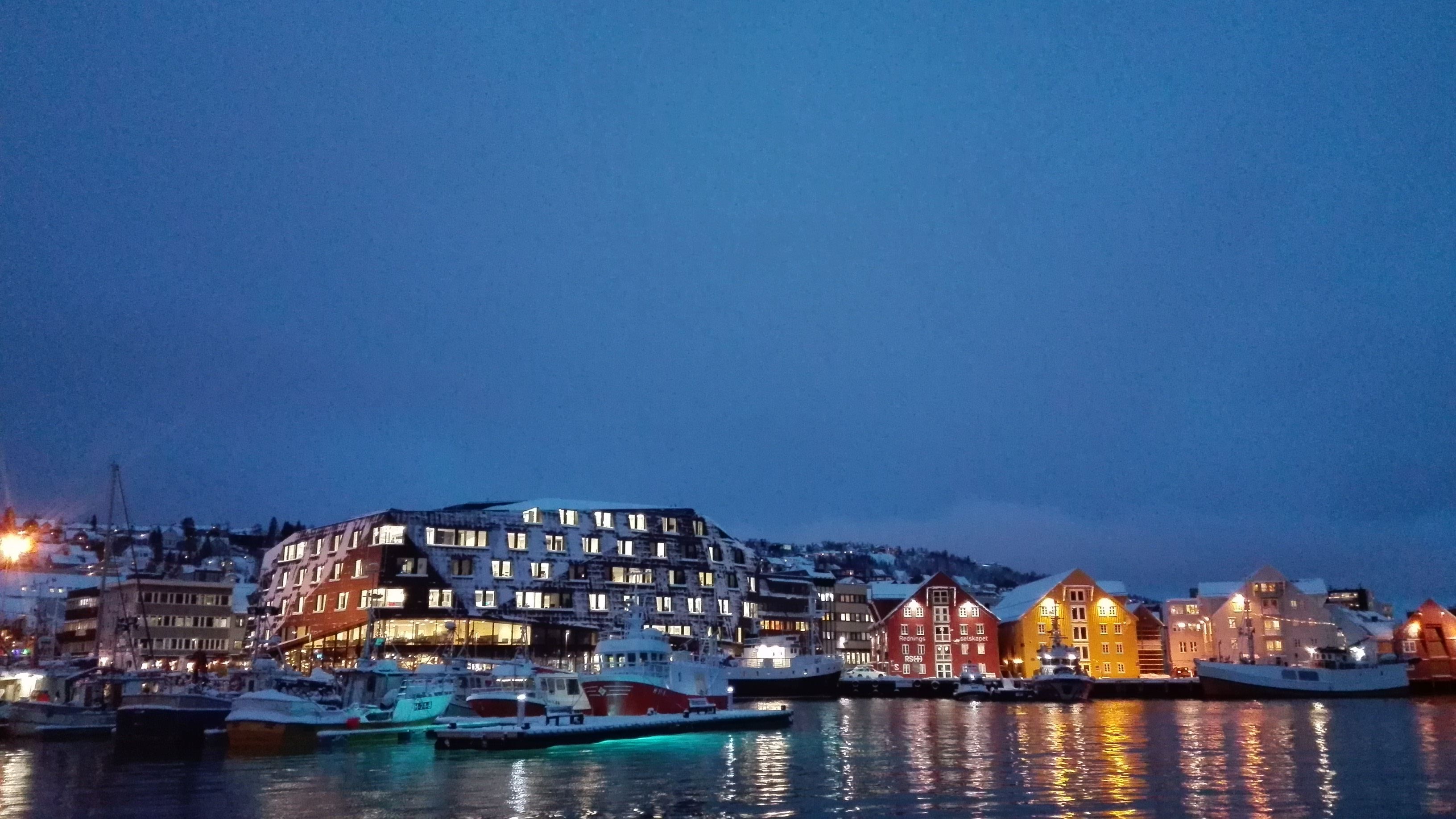 Evening atmosphere by the harbour with boats and illuminated buildings.