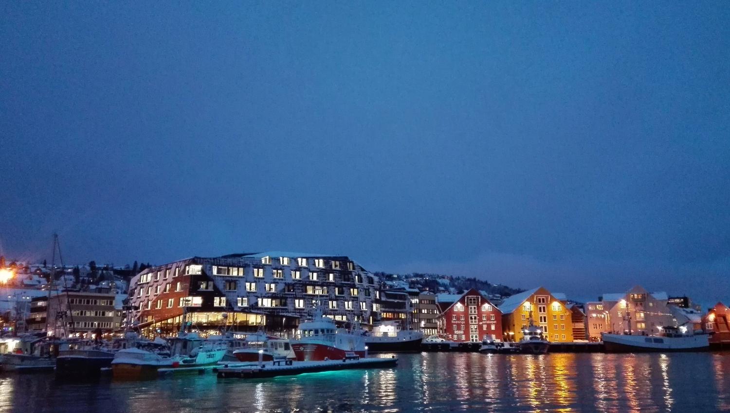 Evening atmosphere by the harbour with boats and illuminated buildings.