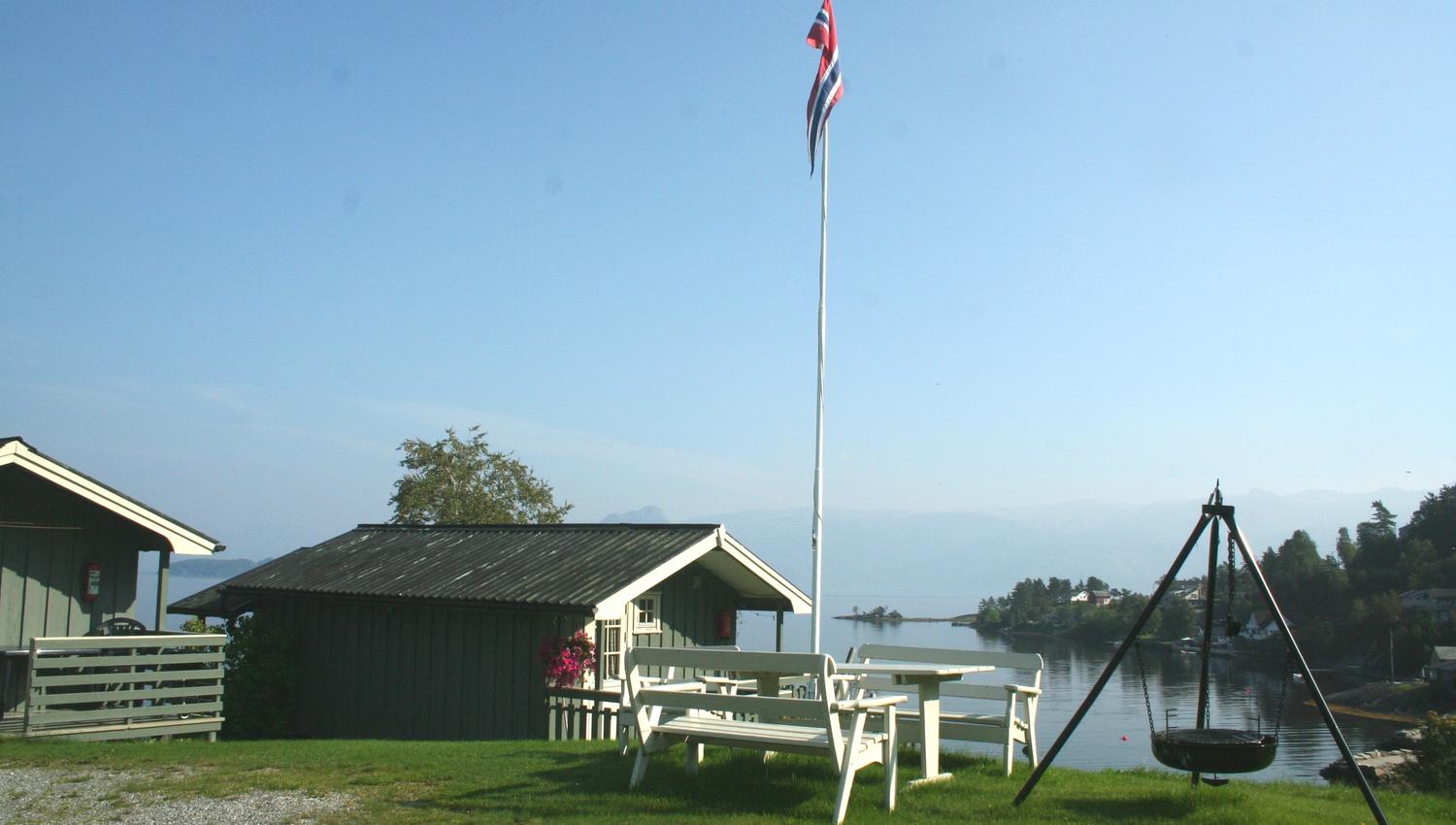 View from Oddland Camping in Hardanger with cabins, a flagpole, and stunning fjord scenery on a sunny summer day.