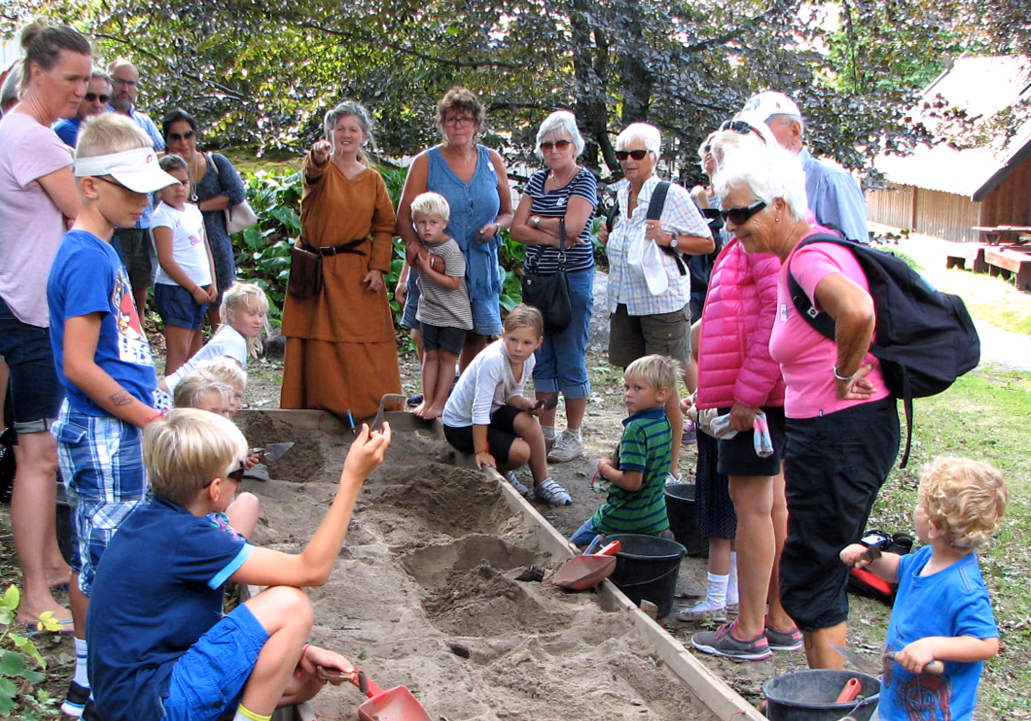 Children and adults stand around a sandbox and dig out objects from the Viking Age.