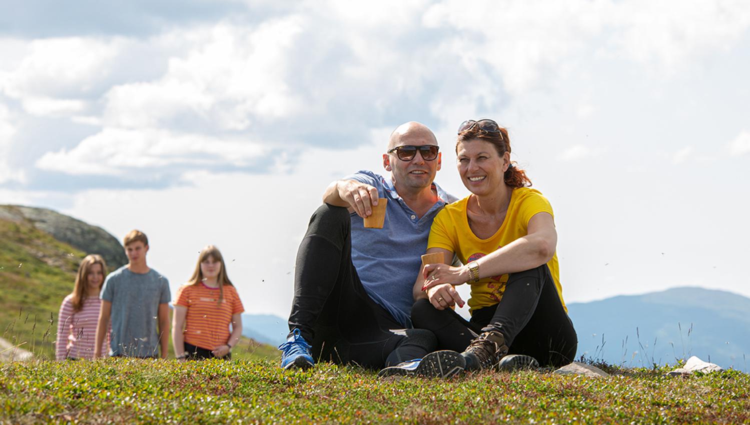 couple sitting on the ground and smiling 2 girls and a boy standing in the background