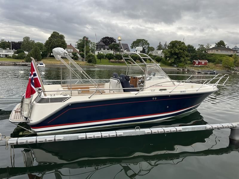 A boat is moored at a dock with houses and gardens along the waterfront.