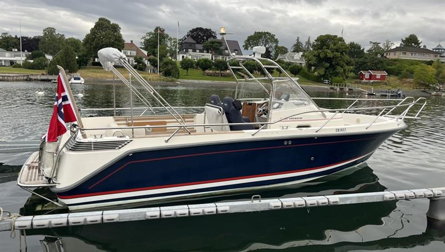 A boat is moored at a dock with houses and gardens along the waterfront.
