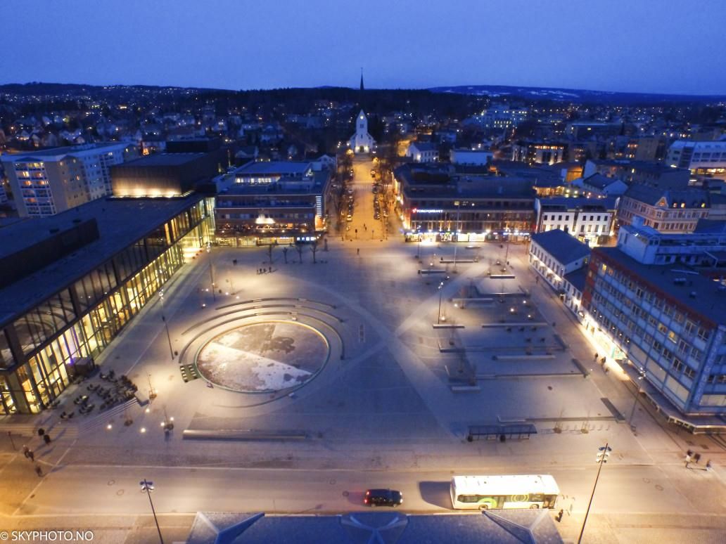 Stortorget in Hamar viewed from above at dusk, with illuminated buildings, clear street lines, and a large open square.