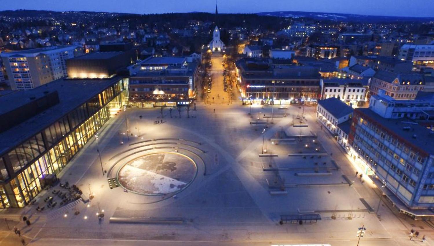 Stortorget in Hamar viewed from above at dusk, with illuminated buildings, clear street lines, and a large open square.