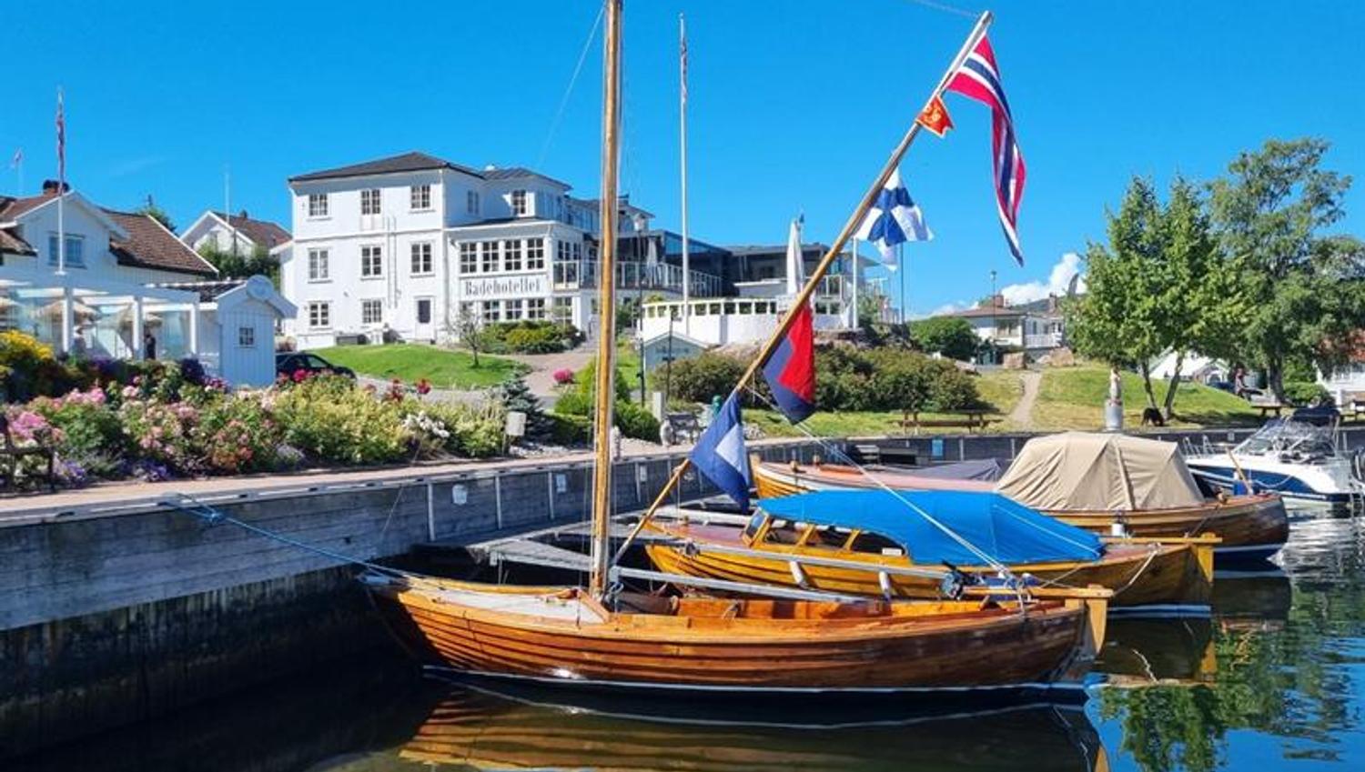 Wooden boats on the water in front of the Badehotellet, blue sky