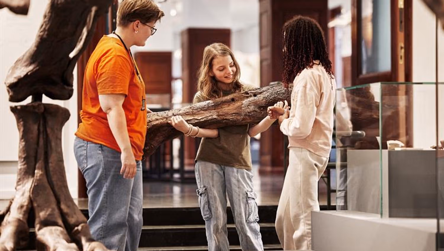 Three children examine a large fossil in a museum with guidance from an adult.