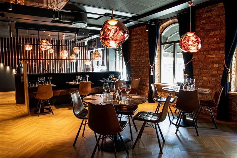 Restaurant interior with round, brown tables, brown chairs and seating section against the wall.