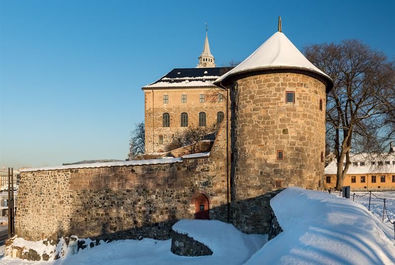 Winter photo of Munk's Tower with the Castle in the background. The ground is covered in snow.