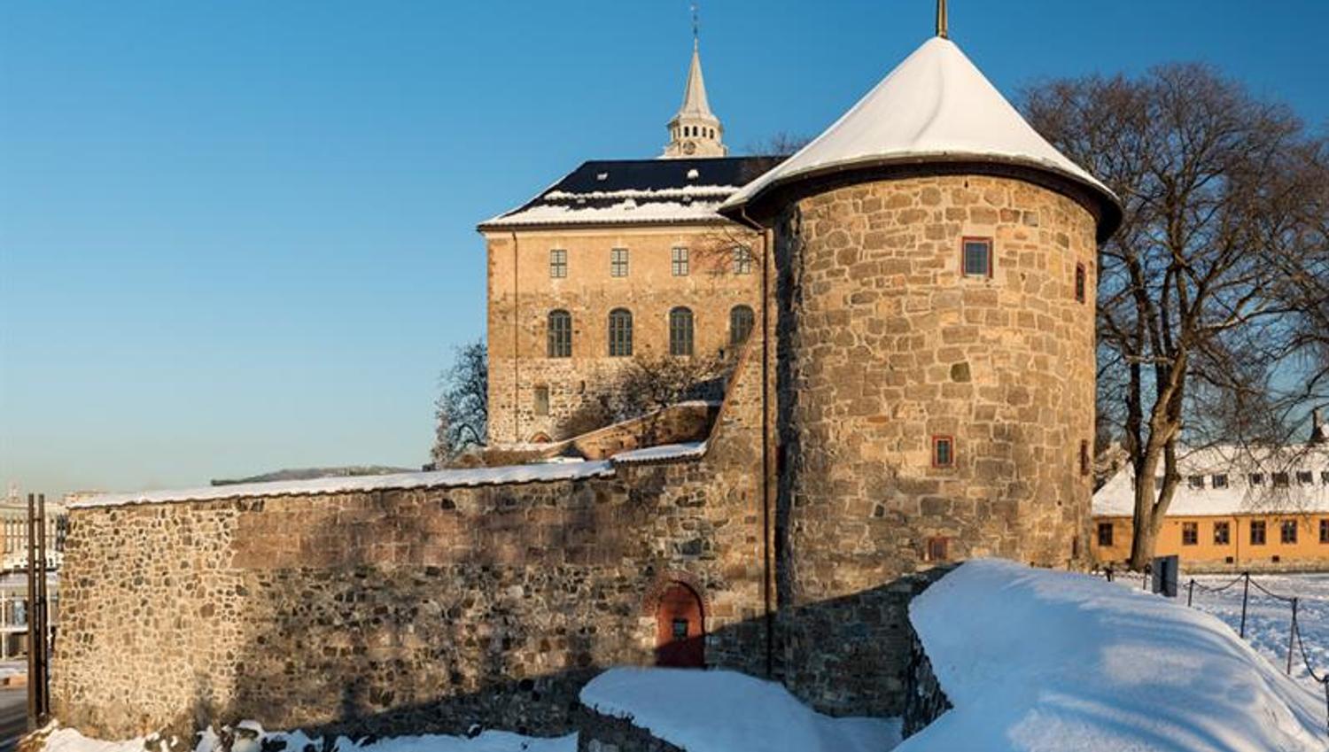 Winter photo of Munk's Tower with the Castle in the background. The ground is covered in snow.