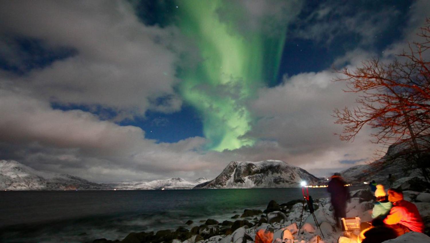 Few guests near a bonfire enjoying the northern lights