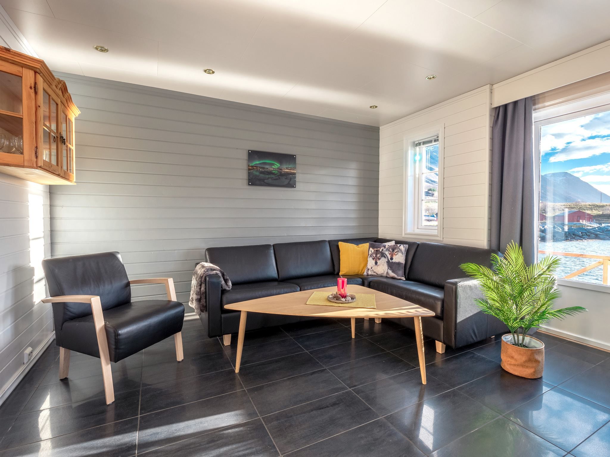 Modern living room with a black leather sofa, wooden coffee table, and a picture of the Northern Lights above the sofa