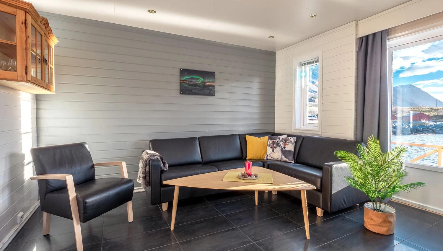 Modern living room with a black leather sofa, wooden coffee table, and a picture of the Northern Lights above the sofa