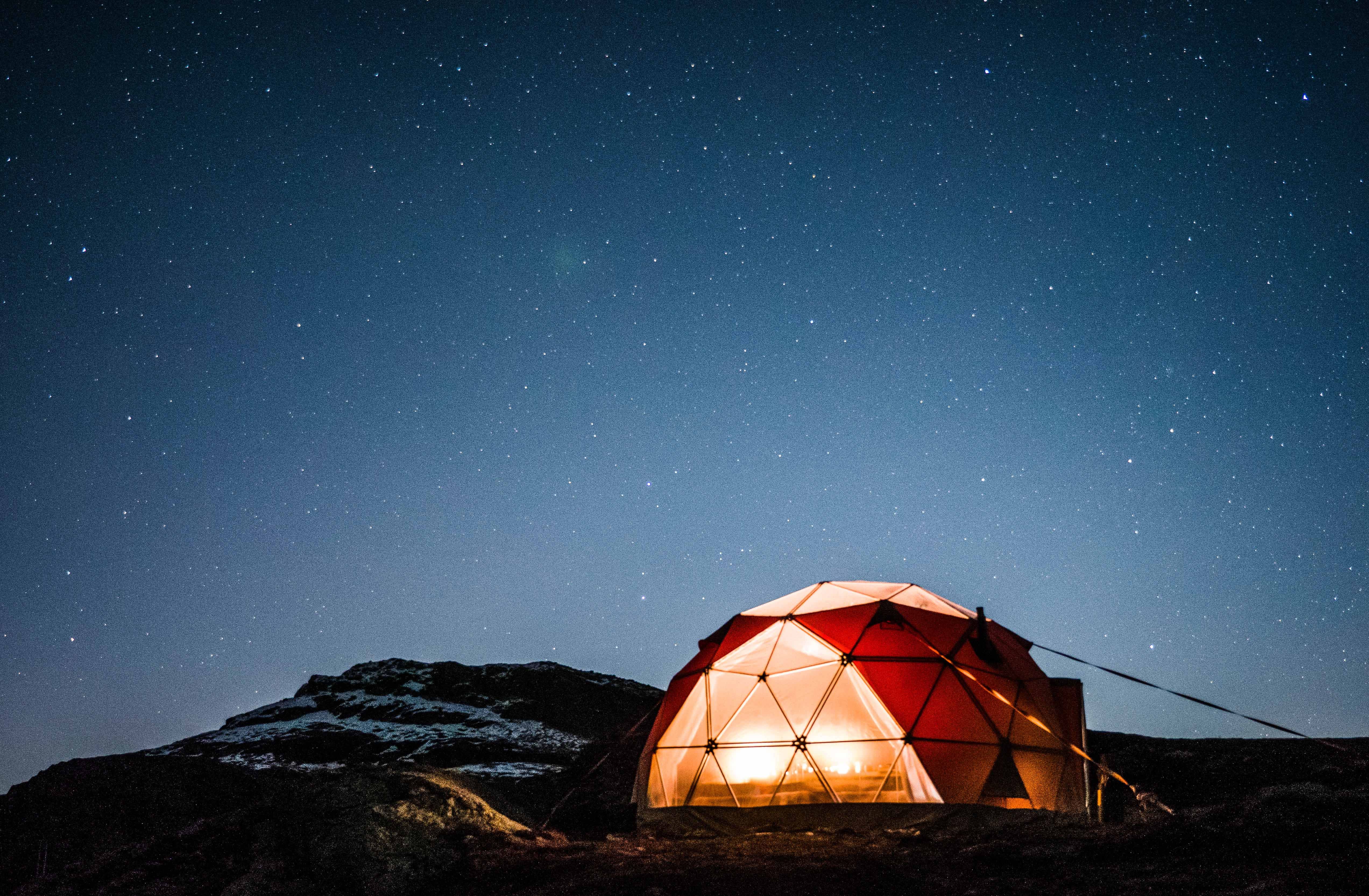 Heated geodome glowing warmly in the winter landscape near Trolltunga beneath a clear night sky.