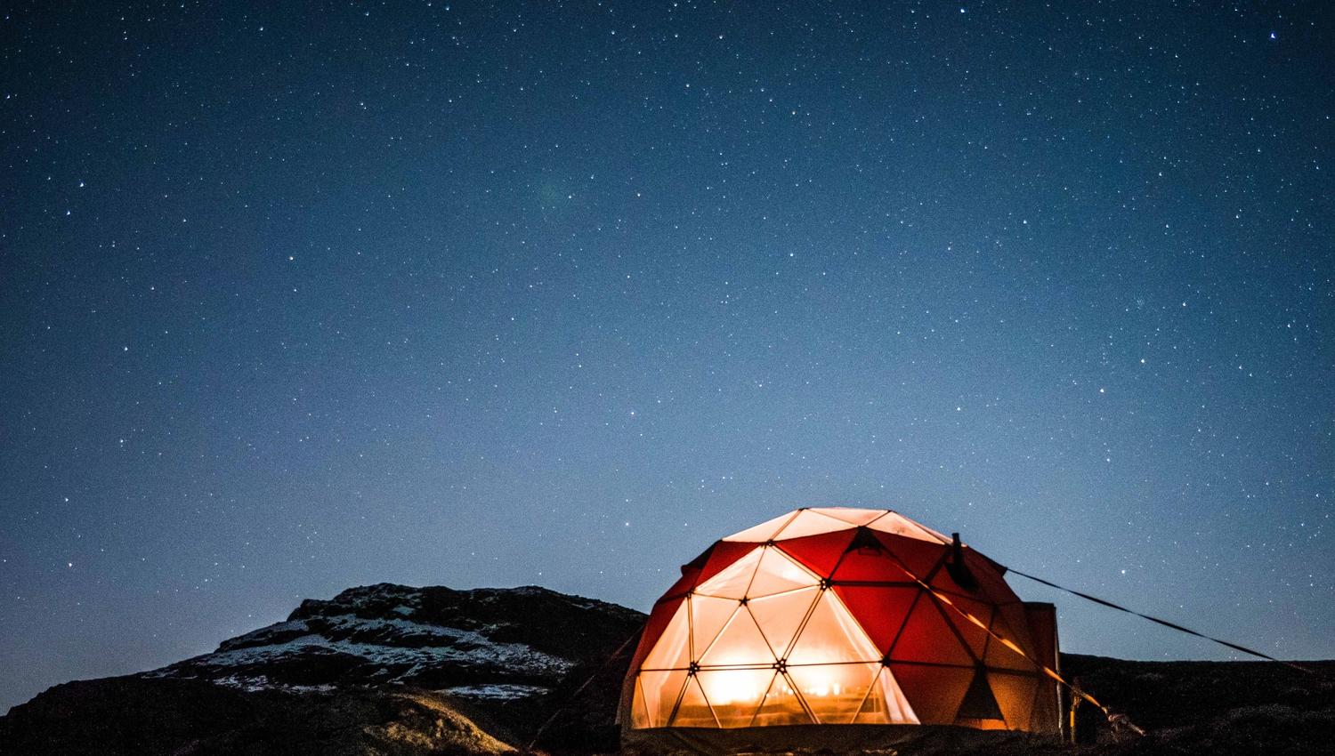 Heated geodome glowing warmly in the winter landscape near Trolltunga beneath a clear night sky.